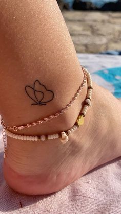 a woman's foot with a heart tattoo on it and two bracelets around her ankles