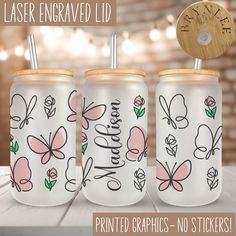 three personalized glass tumblers with flowers and butterflies on them, one has a wooden lid