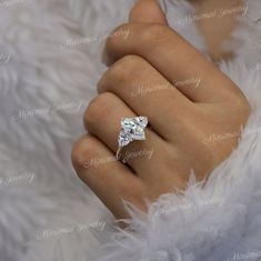 a woman's hand with a diamond ring on top of her finger and white feathers in the background