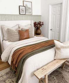 a white bed with pillows and blankets on top of it next to a wooden bench