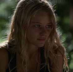 a woman with long blonde hair and blue eyes looks at the camera while sitting down