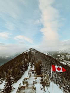 a canadian flag flying on top of a snow covered mountain next to benches and trees