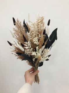 a person holding a bunch of dried flowers in their hand with white and black feathers