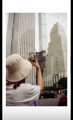 a woman taking a photo with her cell phone in front of tall buildings on a city street