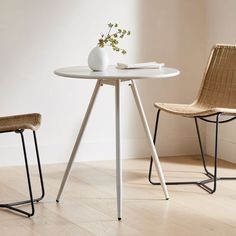 two chairs and a table with a vase on it in front of a white wall