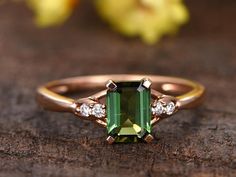 an emerald and diamond ring sitting on top of a piece of wood with flowers in the background