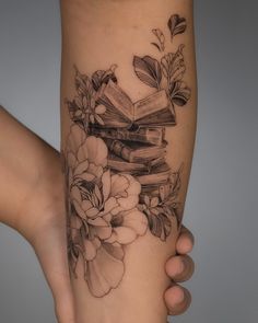 a woman's leg with flowers and books tattoo on her legs, while holding a book in her left hand