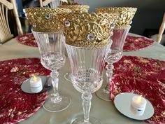 three glass goblets sitting on top of a white tablecloth covered table with candles