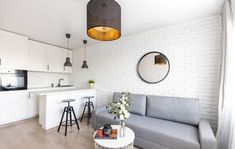 a living room filled with furniture next to a white kitchen and dining table in front of a brick wall