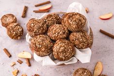 muffins in a basket with cinnamon and apple slices around them on a table