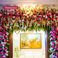 an archway decorated with flowers and greenery in front of a painting on the wall