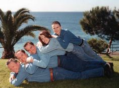 a group of people laying on top of each other in the grass next to water