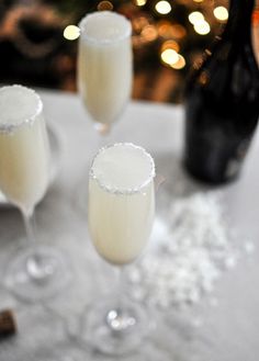 three champagne flutes sitting on top of a white table next to a bottle of wine