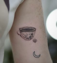 a small tattoo on the arm of a woman with a coffee cup and crescent moon