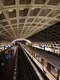 a subway station with people walking on the platform and one train pulling up to it