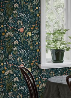 a table and chair in front of a window with a green wallpaper pattern on it