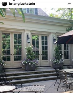 an outdoor dining area with tables and chairs under an umbrella in front of a house