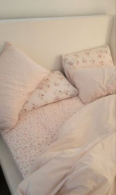 an unmade bed with white sheets and pink flowers on the comforter is shown