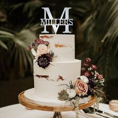 a three tiered wedding cake with flowers on the top and initials on the side