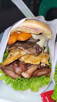 a large sandwich with meat, cheese and lettuce wrapped in paper on a plate