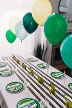 some balloons are hanging from the ceiling above a table with green and white plates on it