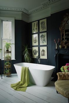 a white bath tub sitting in a bathroom next to a window with pictures on the wall