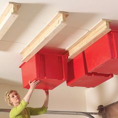 a woman standing on a step ladder holding two red bins above her head, with the bottom planks removed