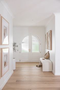 a white entryway with wooden floors and framed pictures on the wall, along with a bench