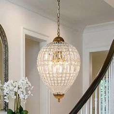 a chandelier hanging from the ceiling in a foyer with white flowers and greenery