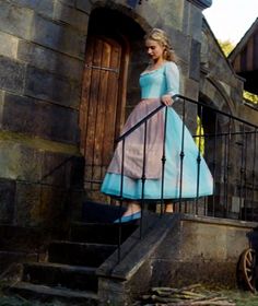 a woman in a blue dress walking up some stairs