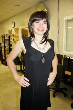 a woman in a black dress standing with her hands on her hips and smiling at the camera