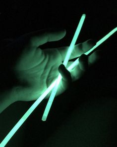 two hands holding glowing sticks in the dark