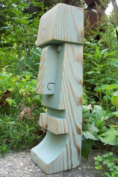 a wooden sculpture sitting on top of a cement ground in front of some bushes and trees