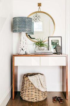 a white table with a mirror and a basket on it next to a wall mounted plant