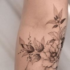 a woman's leg with flowers and leaves tattoo on her thigh, which is black and white