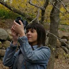 a woman holding a camera up to take a picture in front of some rocks and trees