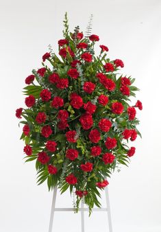 red flowers are arranged on a white stand with green leaves and stems in the center