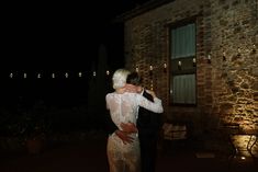 a man and woman dance in front of a brick building at night with string lights