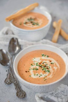 two white bowls filled with soup on top of a table next to silver spoons