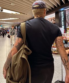 a man with tattoos is pulling his luggage through an airport terminal as people walk by