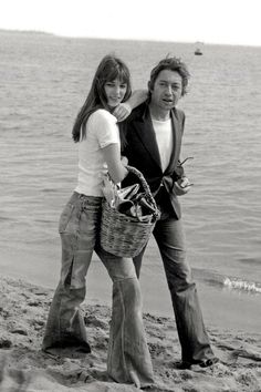 black and white photograph of two people walking on the beach with a basket in hand