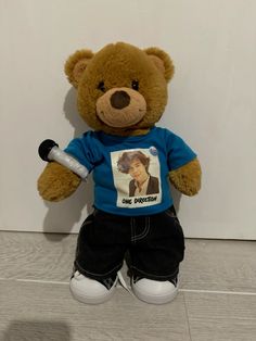 a brown teddy bear wearing a blue shirt and black pants holding a tennis racquet