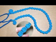 a hand holding a blue crochet necklace with a knot on it's end