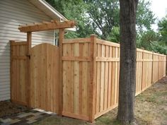 a wooden fence in front of a house next to a tree and grass covered yard