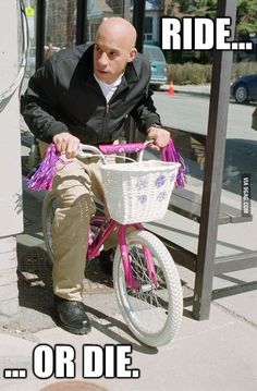 a man riding a pink bike down a street next to a sign that says ride or die