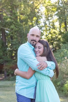 a man and woman hugging each other in front of the camera with trees behind them