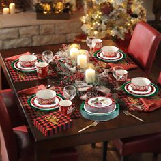 a dining room table set for christmas with red and green placemats, plaid napkins, silverware and candles