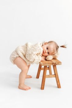 a baby is playing on a stool with her legs spread out to reach the table