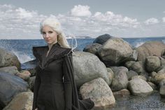 a woman with white hair standing on rocks near the ocean