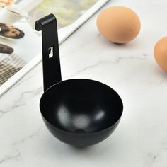 an egg is sitting in a black bowl next to eggs on a counter top with a cookbook and utensils behind it